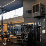 Interior de uma academia moderna com equipamentos de musculação, espelhos, iluminação em LED e homens treinando em um ambiente amplo e arejado.