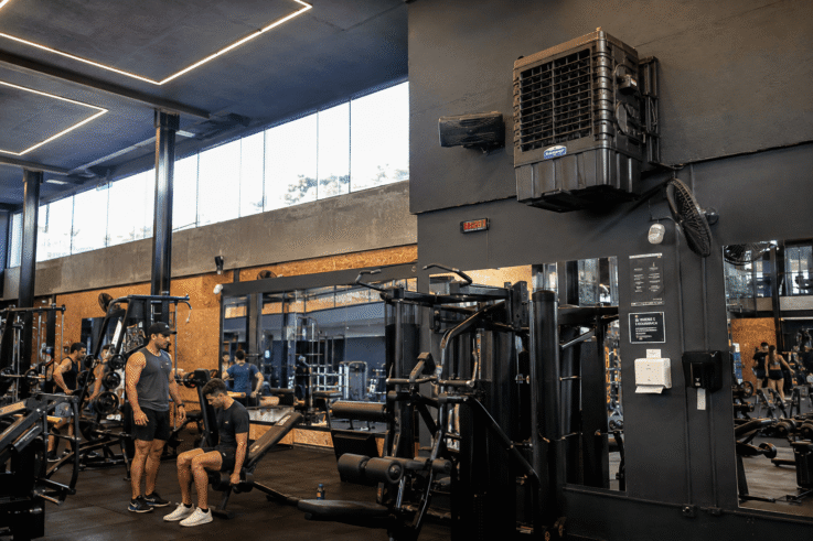 Interior de uma academia moderna com equipamentos de musculação, espelhos, iluminação em LED e homens treinando em um ambiente amplo e arejado.